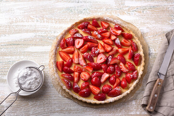 Summer tart with custard of baked milk and juicy fresh strawberries on light wooden background, top view, horizontal