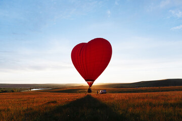 Fototapeta premium hot Red air balloon heart shape flying into sunset over valley landing or taking off