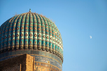 Closeup of the old dome of Bibi-Khanym Mosque over bright blue sky and moon, Samarkand, Uzbekistan