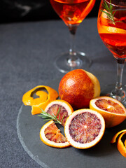 Blood orange slices and whole fruit on dark slate board, orange cocktail in glasses