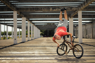 Man in color t-shirt on the bike. Bmx rider performing tricks at street with striped shadow from...