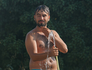 Bearded man douses himself with cool water from a hose after swimming in the sea