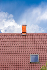 The roof of the house is covered with metal tiles with a roof window and a red brick chimney on the...
