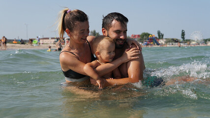 Fototapeta na wymiar Young family hugging in water in sea. Father holding little son in arms