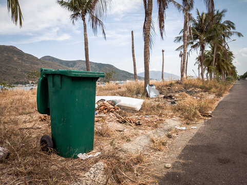 Opened big empty green plastic trash garbage bin in modern comfortable village near sea and palms. Public trash on the side of the road. Infectious control, garbage disposal, disposal of waste concept
