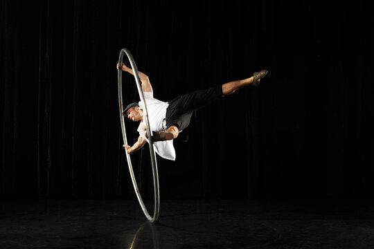 Man in circle. Circus performer artist in a Cyr Wheel (Roy Cyr) in theatre at a black background