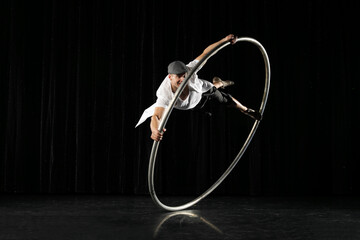 Man in circle. Circus performer artist in a Cyr Wheel (Roy Cyr) in theatre at a black background