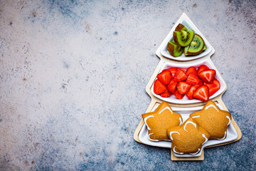 Holiday snacks - gingerbread, kiwi and strawberries on plate Christmas tree, top view, copy space.