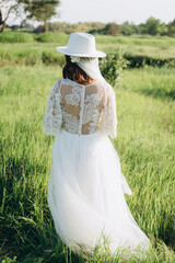 stylish woman in fedora hat  white dress walking in the field with trees