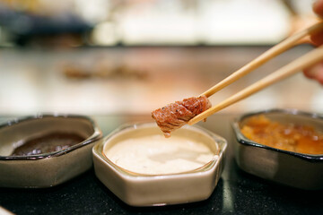 T-bone steak - Hand holding chopsticks to pick grilled beef and dip into mustard sauce, Traditional Japenese teppanyaki.