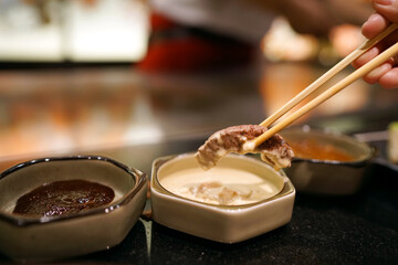 T-bone steak - Hand holding chopsticks to pick grilled beef and dip into mustard sauce, Traditional Japenese teppanyaki.