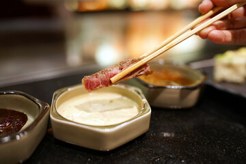 T-bone steak - Hand holding chopsticks to pick grilled beef and dip into mustard sauce, Traditional Japenese teppanyaki.
