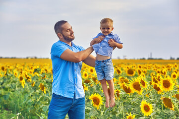 Fototapeta premium Happy father and son on a summer walk in the field with sunflowers . Father's day