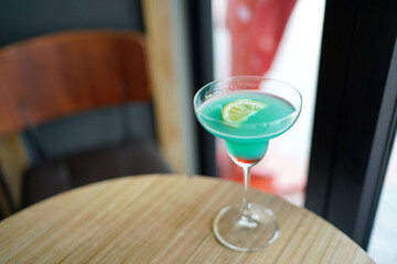 A glass of blue margarita cocktail with raspberry syrup and sliced lime on blurred background and copy space, Bar counter in the club.