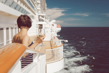 Beautiful lady in striped blue dress on deck of cruise ship with a glass of white wine