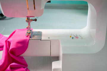 Close up of sewing machine working with pink fabric and pins on a table. Home hobby and business....