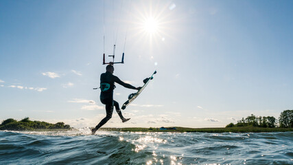 Kitesurfer walking like Jesus on the water with Kiteboard in his hand and backlit by the bright sun