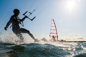 Kitesurfer and windsurfer having fun on the water while backlit from the sun