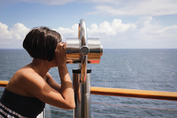 Beautiful woman with hair style and  in blue striped dress looking through binoculars at the cruise ship