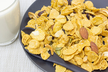 Cornflakes on a black plate and fresh milk in a clear glass and black spoon ready to serve as breakfast