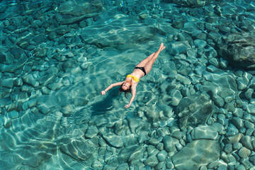 A woman swims in blue sea water in the bay. Nature and relaxation, top view