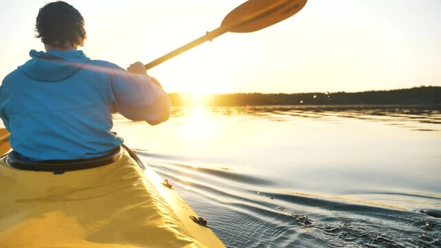 young man in a blue jacket paddles a kayak on the lake at sunset, outdoor activities close-up