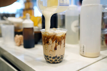 Bubble Milk Tea - Pouring cream cheese into glass of milk tea with black sugar syrup (Kuromitsu)...