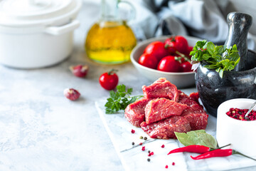 pieces of chopped raw fresh meat fillet on a white marble background. Tomatoes, chili peppers and herbs for cooking. Copy space