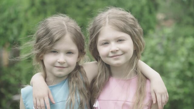 Two pretty little girls hugging and smiling at camera outdoors. Portrait of charming twin sisters posing on summer day. Leisure, beauty, lifestyle, childhood.