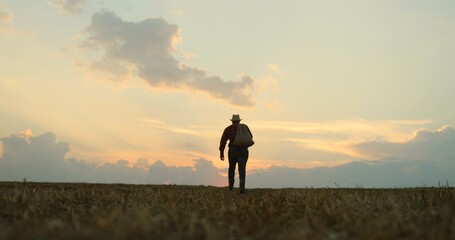 Silhouette of the man with a sack full of the harvest over his back going away to the horizon in the field.