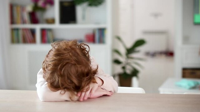 cute redhead kid, boy making funny face while sitting at the table in the living room