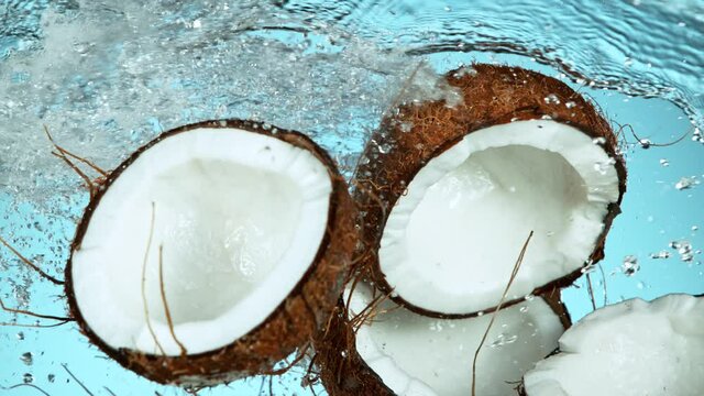 Super Slow Motion Shot of Flying Fresh Coconuts and Water Side Splash on Light Blue Background at 1000fps.