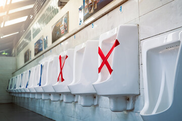 White ceramic urinals in men public toilet. Social distancing in men restroom to prevent...