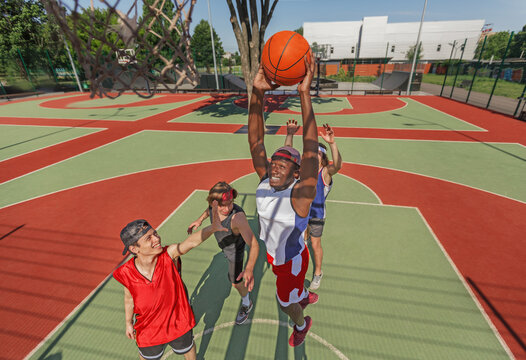 Black basketball player jumping to score goal and his team at outdoor court - Powered by Adobe