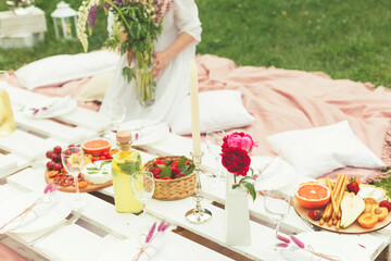 Cut view of young florist woman decorating festive summer picnic for wedding or birthday celebration in pink colors in the garden. Food and drink concept. Selective focus