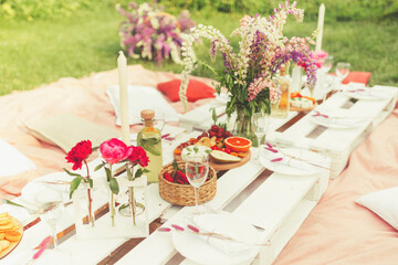 Beautiful festive summer picnic with tasty snacks, fruits and cold drinks, decorated with flowers and candles in pink colors for hen-party. Event agency. Selective focus