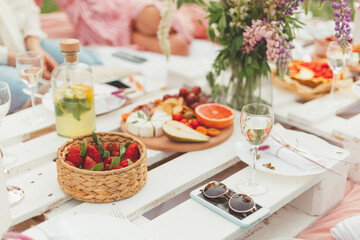 Group of friends enjoying tasty food and drinks at summer festive picnic. Selective focus. Pleasure time. Floristic decorations
