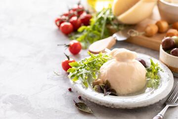Italian cheeses burrata, mozzarella, scorocia, boccini with olives, cherry tomatoes and arugula on a round white plate on a light background. Copy space
