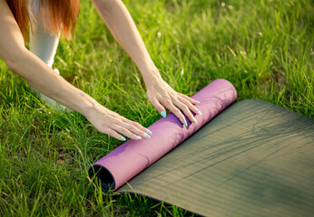 Woman fold up mat after yoga workout close up in the park Healthy life