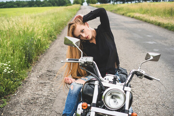 Attractive biker girl looks in a rear view mirror of her motorcycle