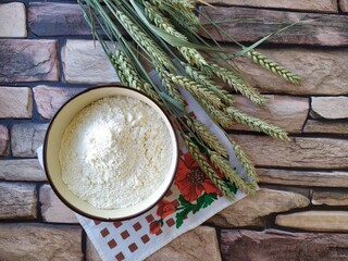 Wheat ears and a bowl of flour on a brick background