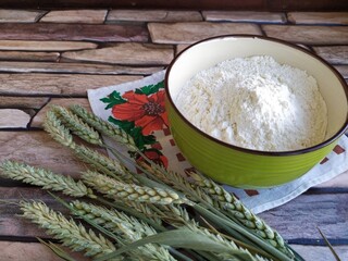 Wheat ears and a bowl of flour on a brick background