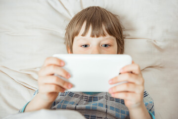 Modern little child lies on bed with smartphone in his hands. Addiction on gadgets concept