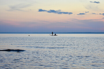Two people swim in the sea on a surf with a paddle at sunset