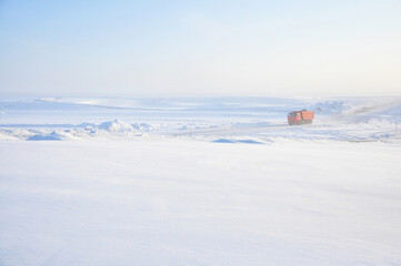 Red truck driving on ice road on Lena river after storm. Minimalist industrial landscape