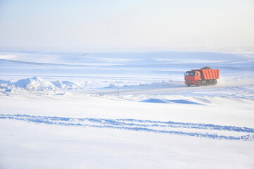Red truck driving on ice road on Lena river after storm. Minimalist industrial landscape