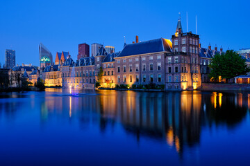 Fototapeta premium View of the Binnenhof House of Parliament and the Hofvijver lake with downtown skyscrapers in background illuminated in the evening. The Hague, Netherlands