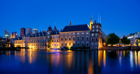 View of the Binnenhof House of Parliament and the Hofvijver lake with downtown skyscrapers in background illuminated in the evening. The Hague, Netherlands