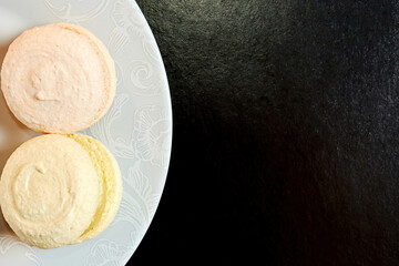 Flat lay template with tasty macaroons on the plate lays on the black surface. Backdrop with copy space for advertisement text