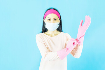 Young Beautiful Asian woman maid wearing face mask  and setting up the latex gloves ,Isolated on blue background,Cleaning Service,housework and household concept.